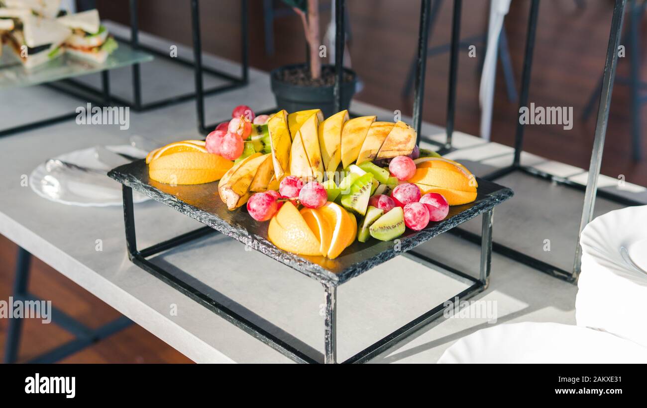 Primo piano di frutta fresca tropicale. Banane, kiwi, arancio e uva sono sul piatto. Concetto di sano servizio di ristorazione e catering Foto Stock