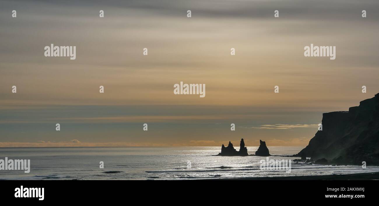 Vik spiaggia al tramonto, Islanda, con pile di mare e la scogliera sulla bassa orizzonte e moody giallo sera cielo invernale Foto Stock