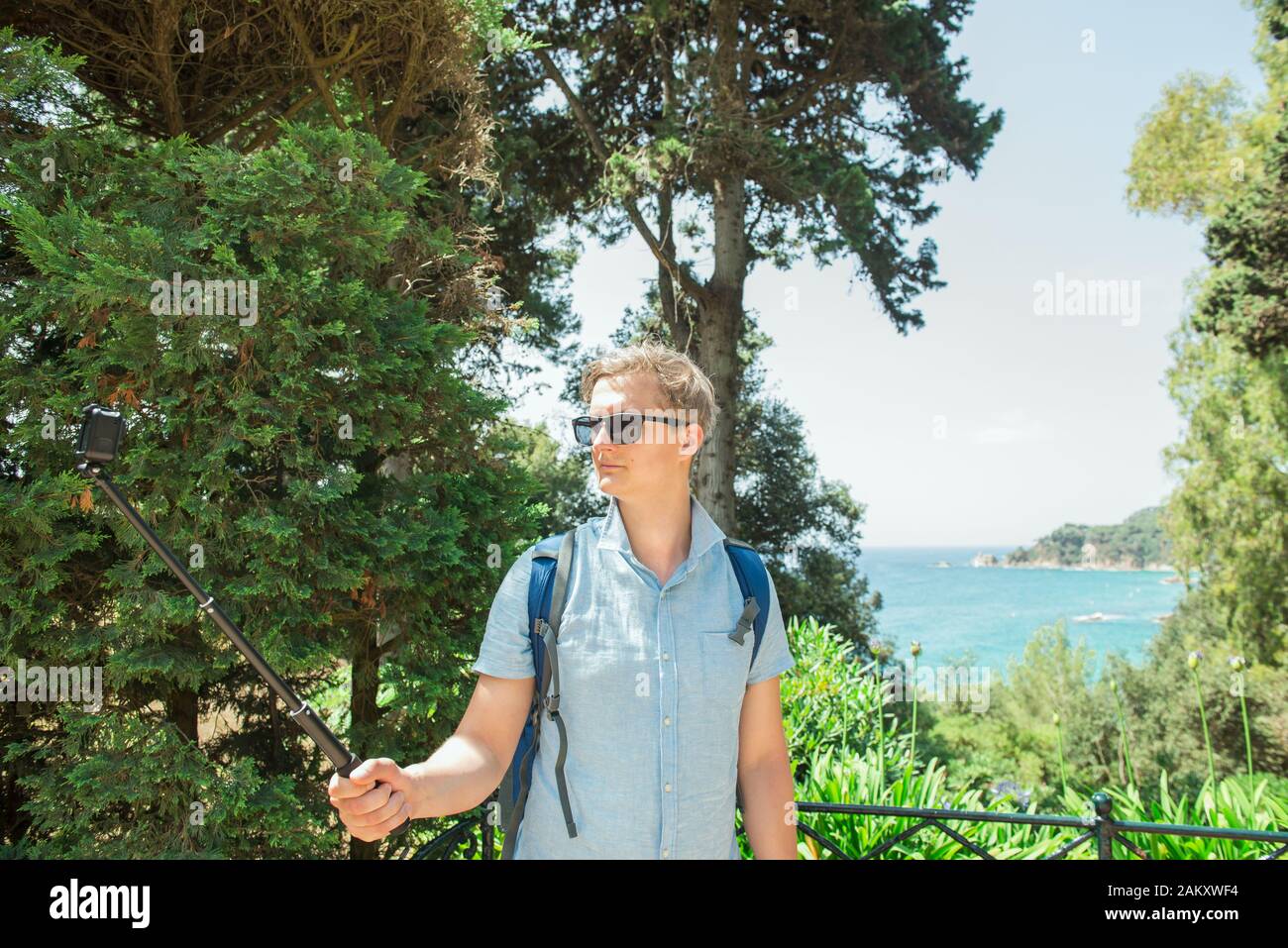 Giovane uomo che fa foto e video di posizione verde con sfondo mare con fotocamera compatta d'azione. Fotocamera collegata al selfie stick. Nuova tecnologia per Foto Stock