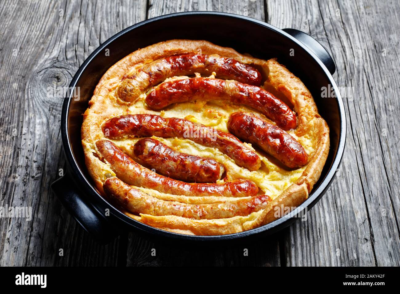 Primo piano di Toad nel buco, Salsiccia Toad, piatto tradizionale inglese costituito da salsicce in Yorkshire pudding paster in ceramica nera da forno Foto Stock