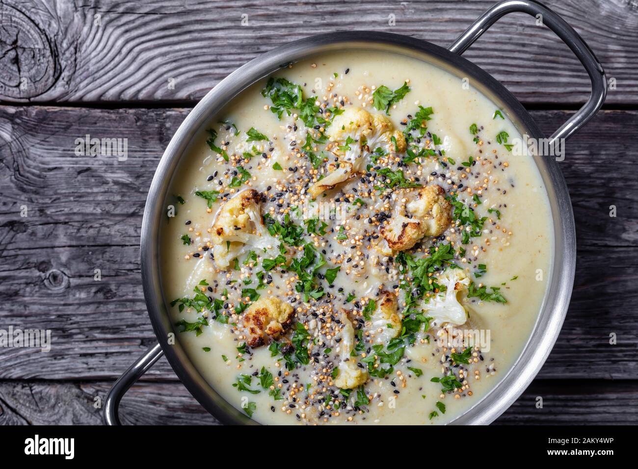 Zuppa cremosa di cavolfiore all'aglio arrosto con formaggio asiago e un croccante di semi di quinoa e chia in una pentola su un rustico tavolo di legno, ho Foto Stock