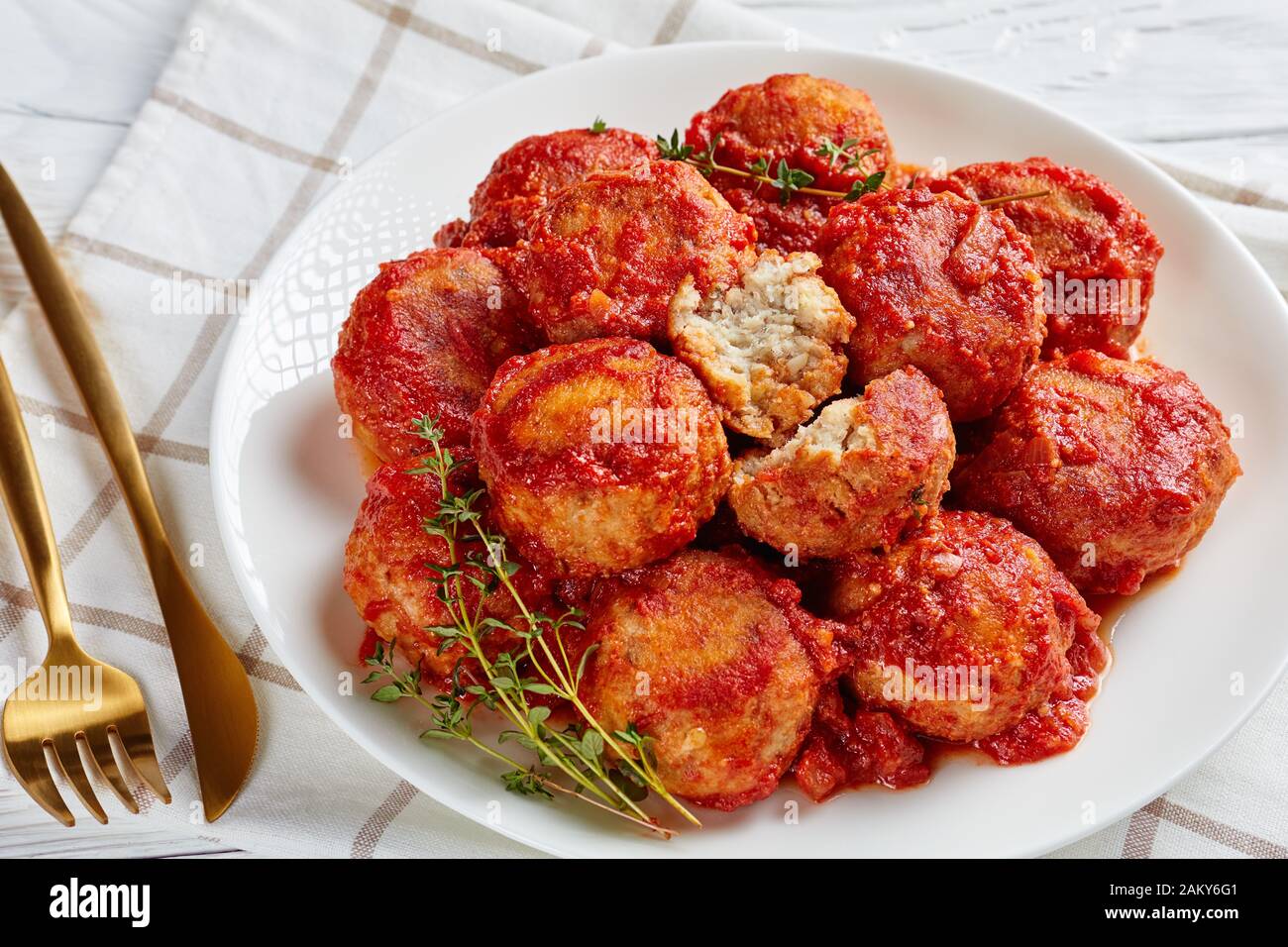 Palle di pesce fritte in salsa di pomodoro su un piatto bianco su un tavolo di legno con forchetta e coltello dorati Foto Stock