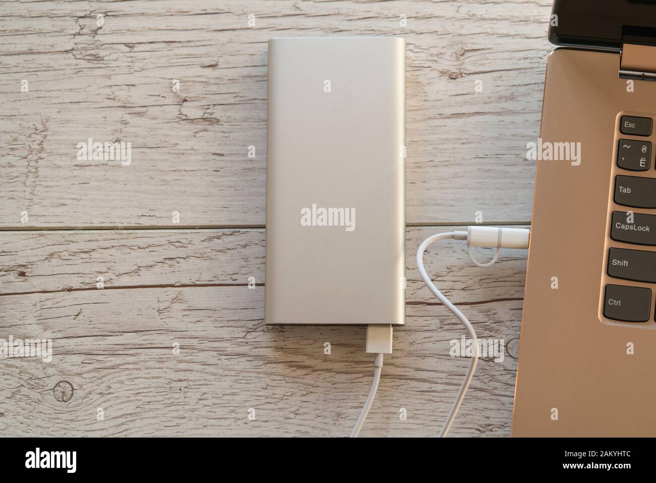 Power bank argento ricarica notebook color oro su schede in legno sfondo. Dispositivo portatile produttivo per viaggi di lavoro. Immagine a colori, direttamente abov Foto Stock