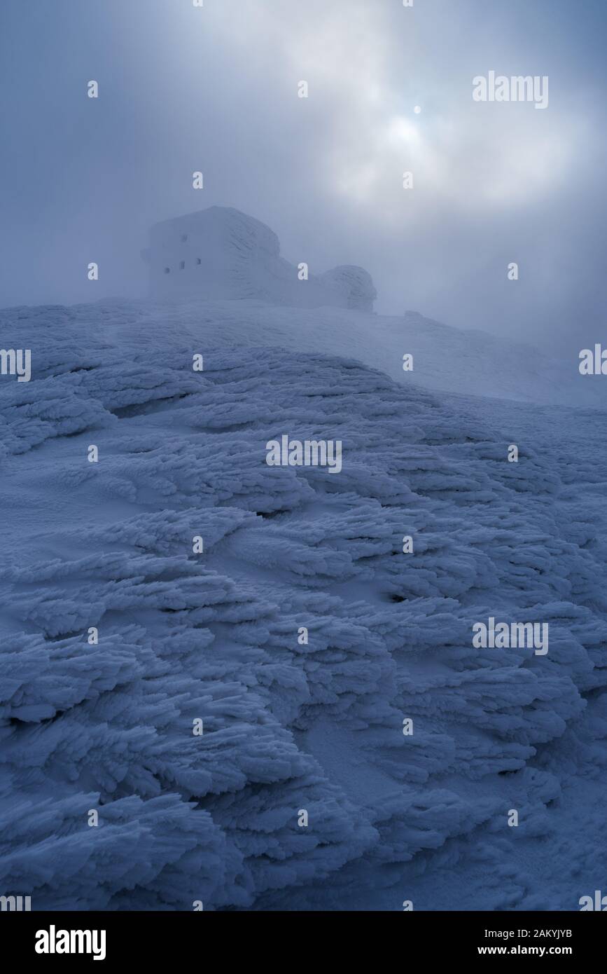 Paesaggio mistico con un vecchio osservatorio abbandonato sulla cima di una montagna. Condizioni meteorologiche invernali gravose con nebbia, nevicate e brina. Carpazi, Ukra Foto Stock