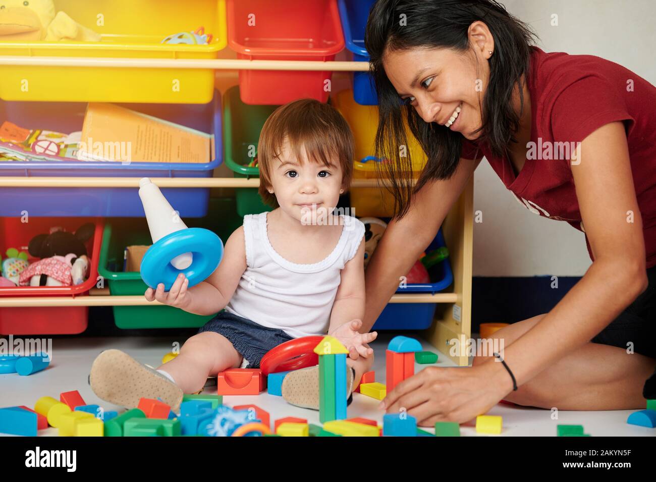 Giovane mamma gioca con baby girl su sfondo di giocattoli Foto Stock