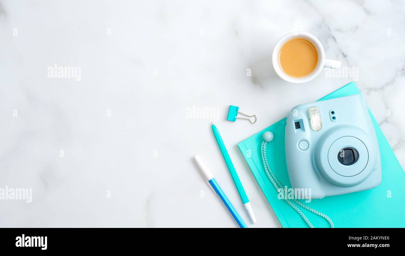Spazio di lavoro femminile con fotocamera istantanea moderna, tazza da caffè, blocco note alla menta, cancelleria su sfondo in marmo. Disposizione piatta, vista dall'alto, spazio di copia. Freelancer h Foto Stock