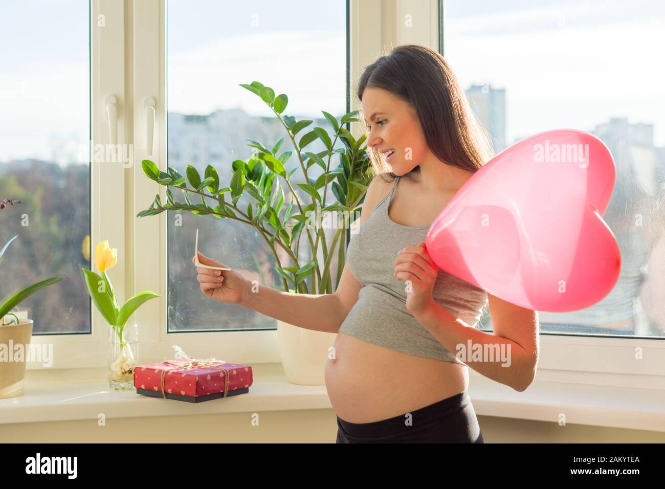 Giovane bella donna incinta con scatola regalo e cuore palloncino rosso,  femmina a casa vicino finestra, San Valentino e vacanze. Maternità e  gravidanza Foto stock - Alamy