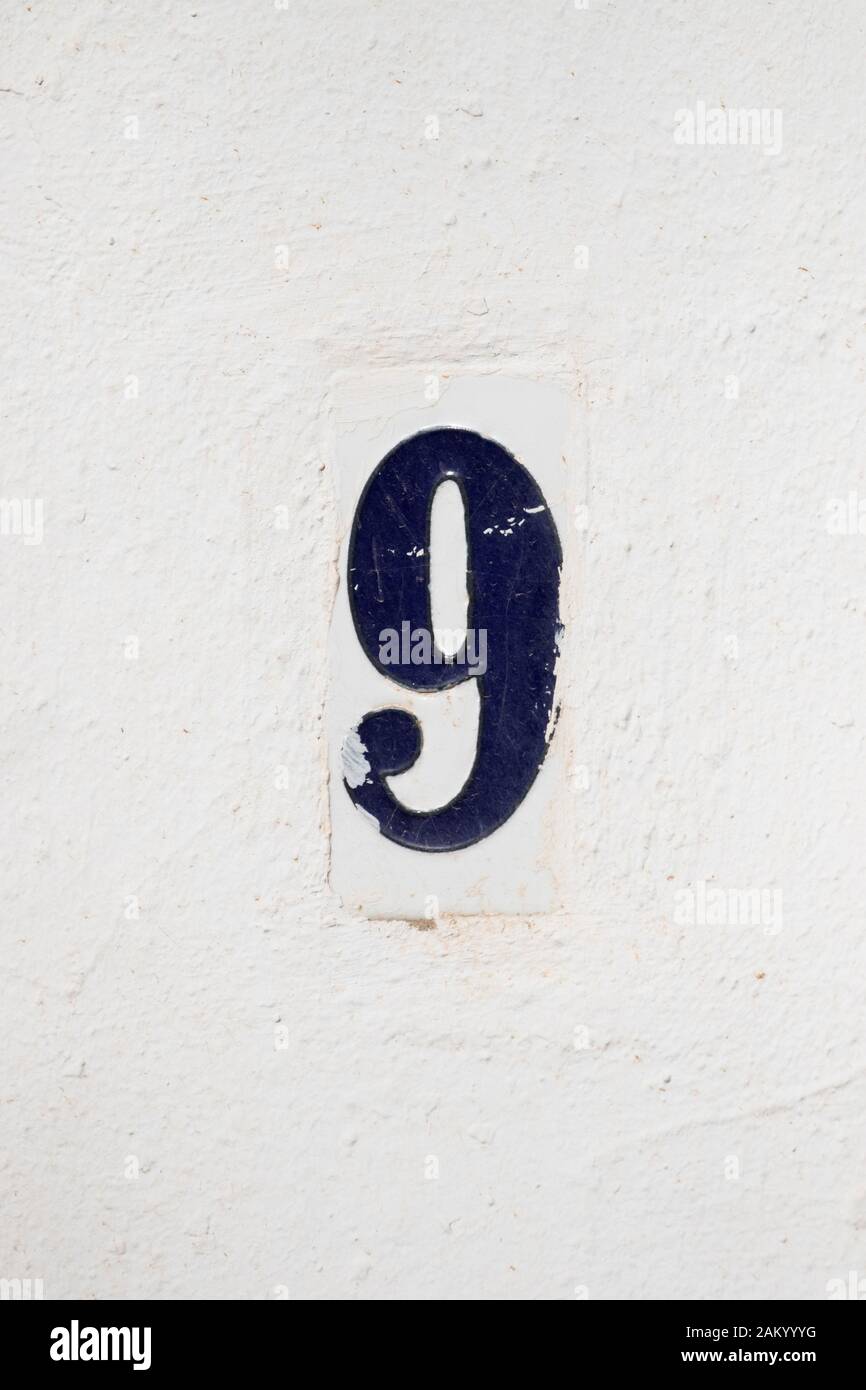 Numero civico 9 blu su un muro bianco Foto Stock