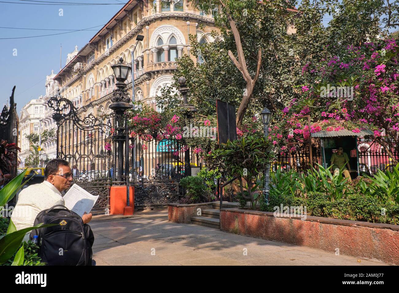 Un uomo legge un giornale a Horniman Circle Garden, Horniman Circle, Fort, Mumbai, India; sullo sfondo: L'edificio in stile veneziano Elphinstone Foto Stock