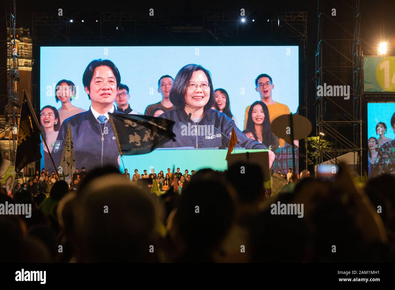 Persone allietare e bandiere d'onda come presidente di Taiwan Tsai Ing-wen e il suo vice candidato presidenziale William Tsai vengono visualizzati su uno schermo dietro di loro sul palco a loro Ketagalan Boulevard comizio elettorale a gennaio 10, 2020, vigilia di Taiwan l'2020 elezioni presidenziali., Taipei, Taiwan, 10 Gennaio 2020 da Perry Svensson Foto Stock