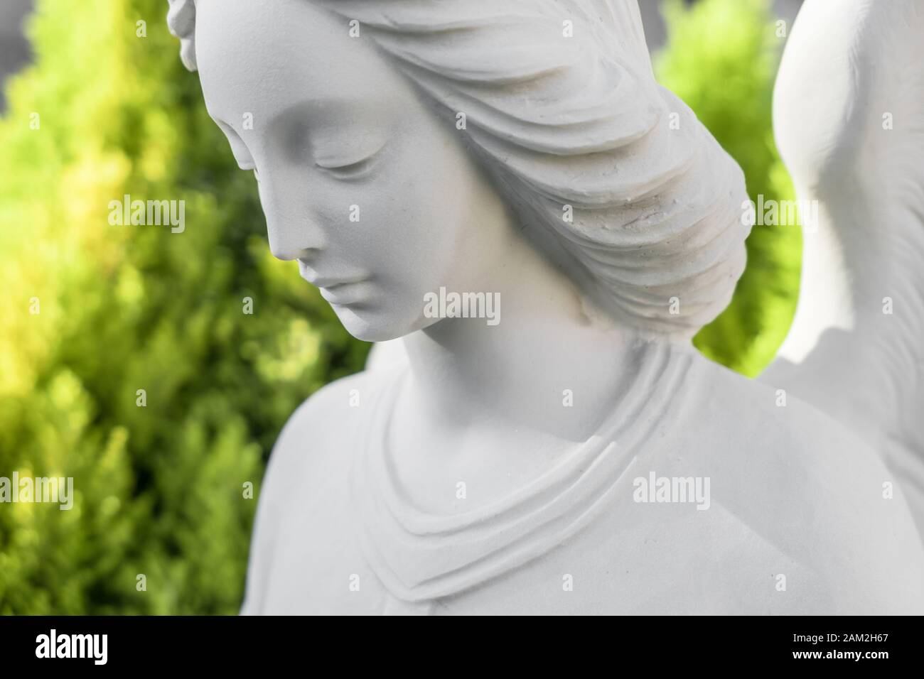 Primo piano della statua di angelo di pietra bianca con sfondo verde sfocato piante. Ideale per concetti e altro. Foto Stock