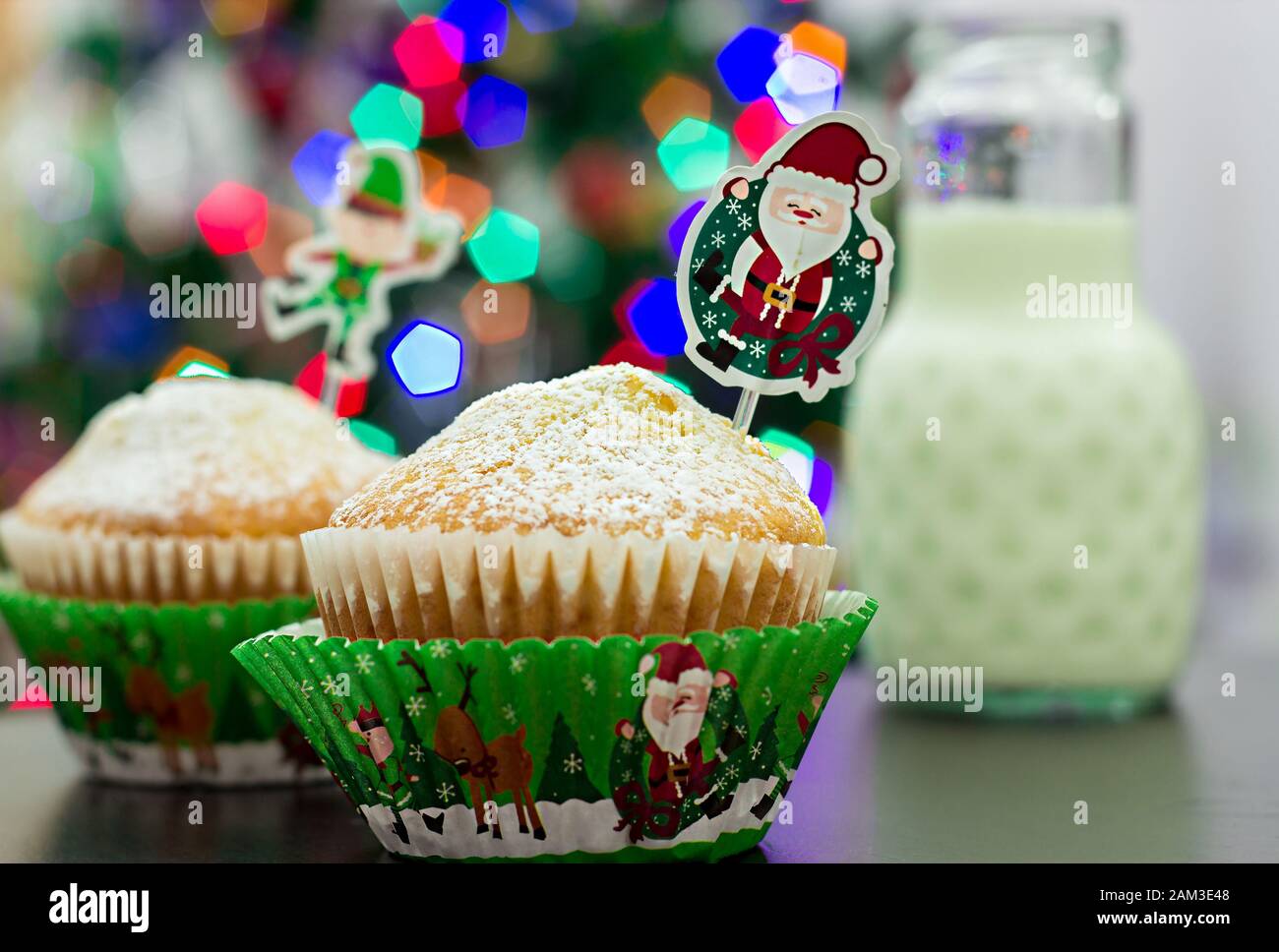 Due muffin in custodie di carta festive, una bottiglia di latte. Capodanno e Natale sfondo sfocato Foto Stock