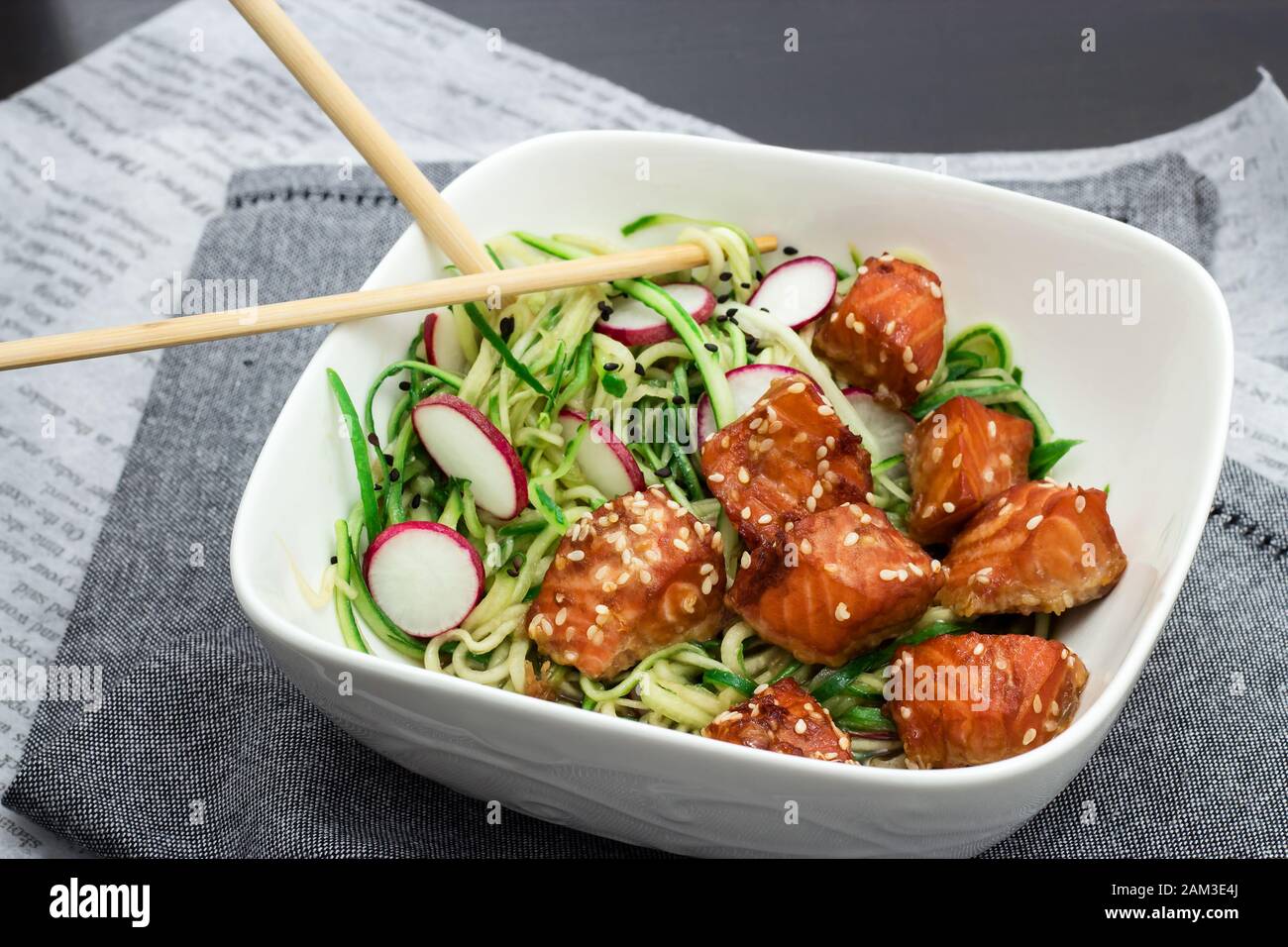 Cucina asiatica salmone alla griglia semi di sesamo cetrioli e spaghetti di rafano insalata ciotola bianca Tovagliolo grigio sfondo nero Foto Stock