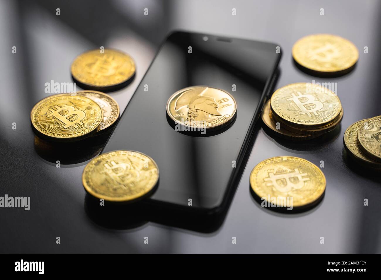 Moneta di bitcoin di titanio dorato su uno smartphone con un sacco di monete di bitcoin su un tavolo. Concetto di criptovaluta virtuale. Estrazione di bitcoins bussiness online Foto Stock