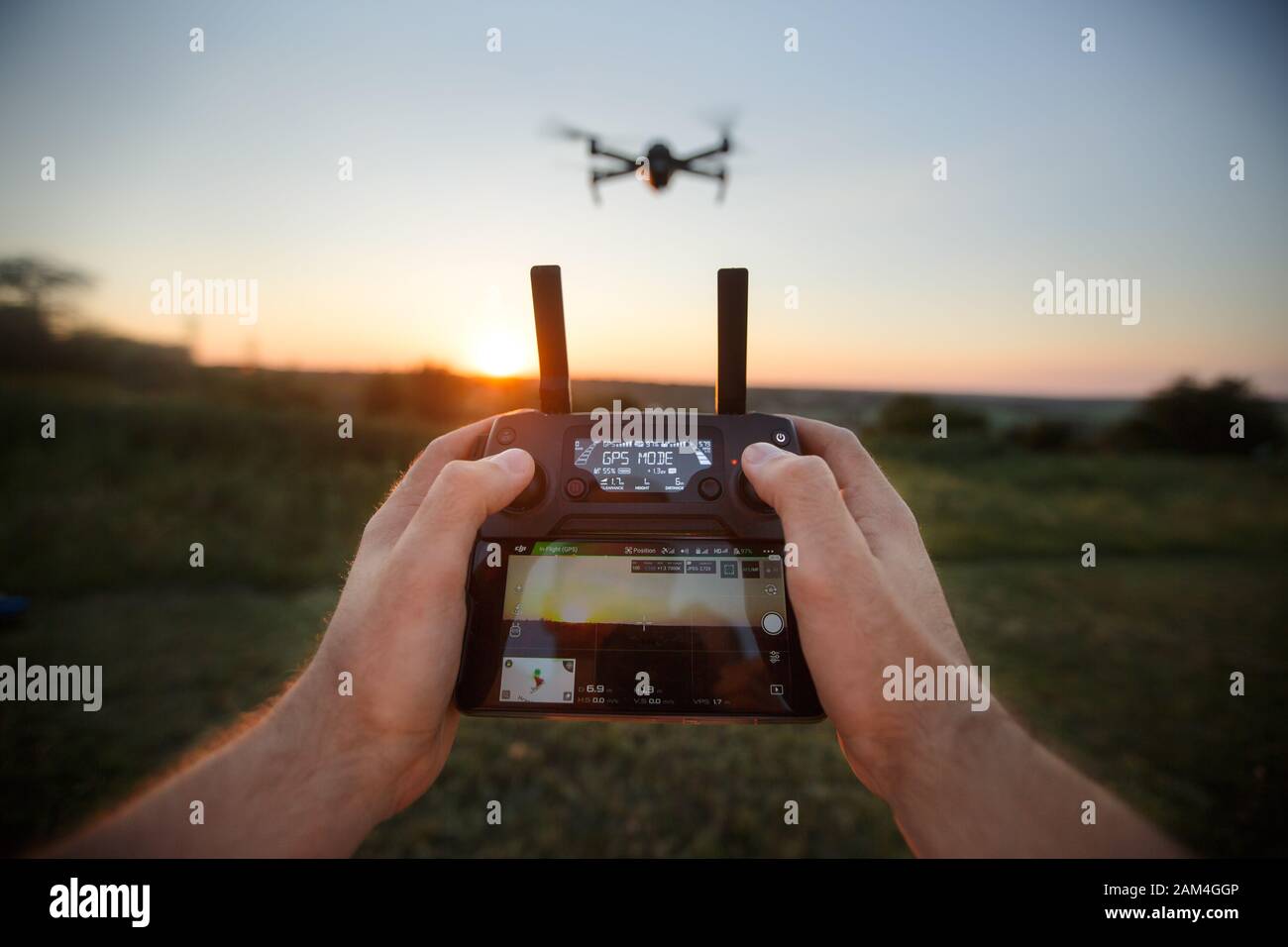 Punto di vista dell'uomo che tiene il telecomando con le mani e scatta foto video aeree. Quadcopter sta volando sullo sfondo. POV - drone Foto Stock