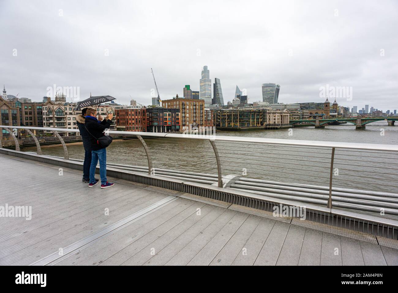 Persone sul Millennium Bridge, Londra in inverno con un ombrello Foto Stock