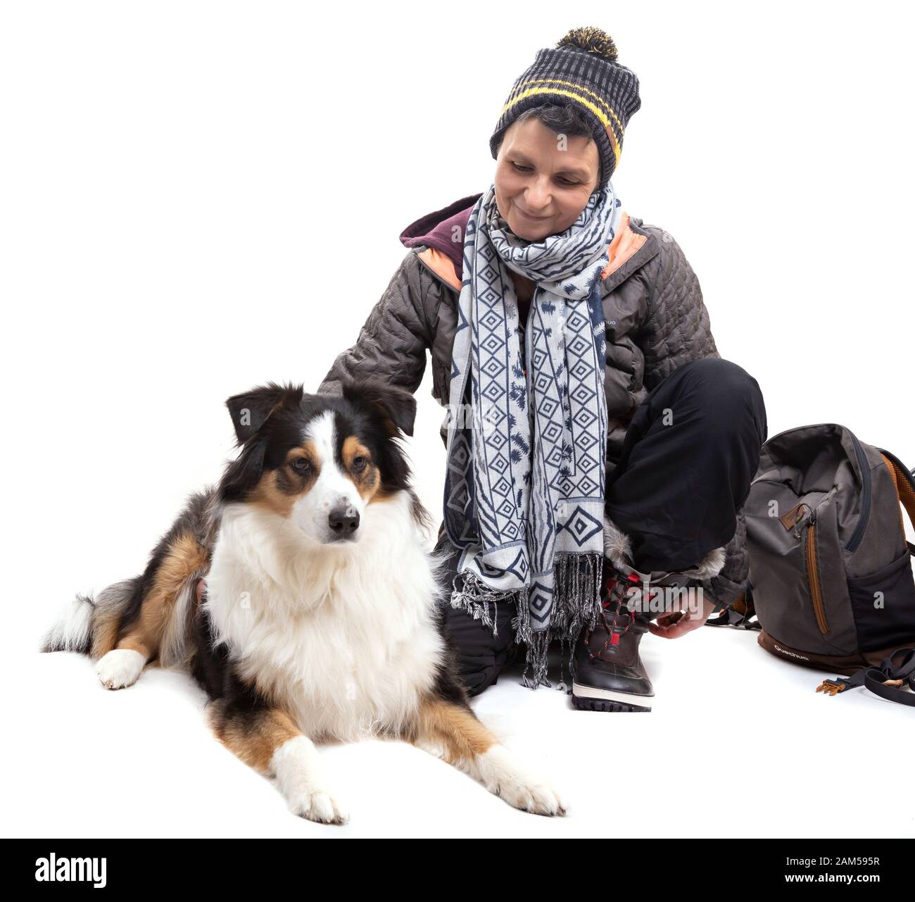 Donna accovacciata che indossa l'abito da trekking invernale su sfondo bianco, con il suo cane Foto Stock