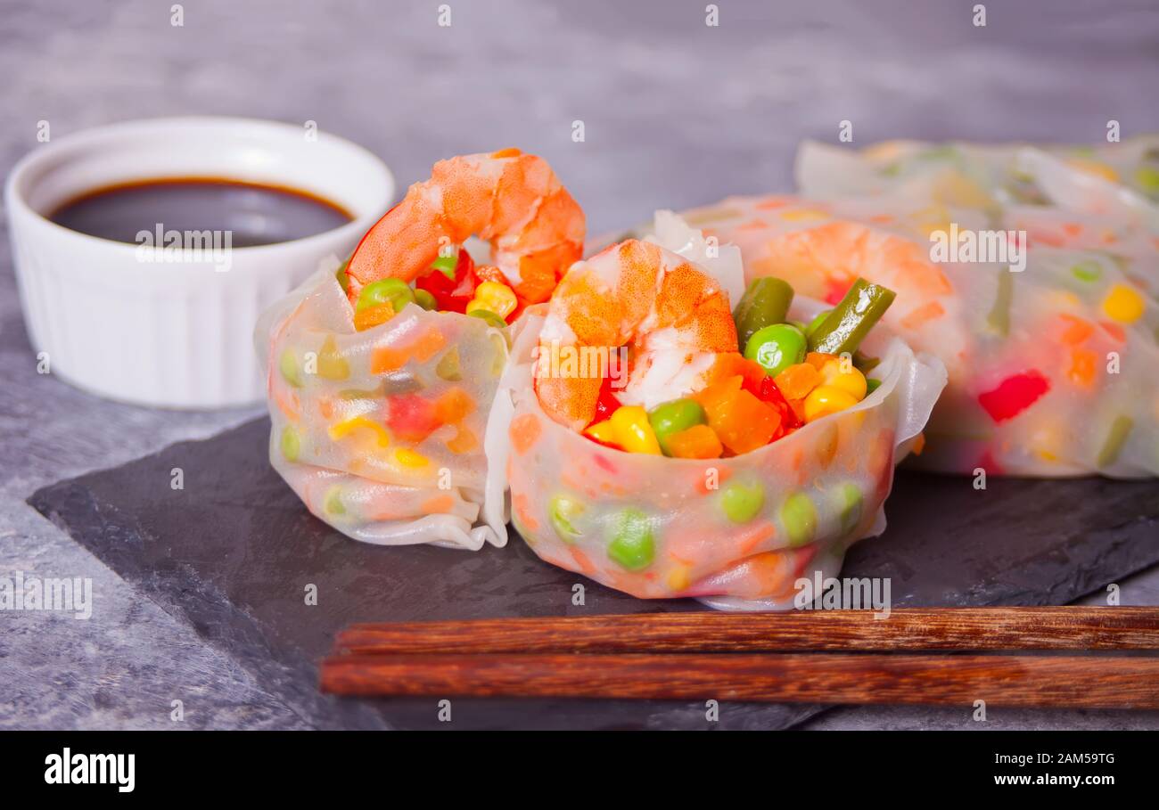 Involtini primavera con verdure e gamberetti in una carta di riso sulla piastra nera. Foto Stock
