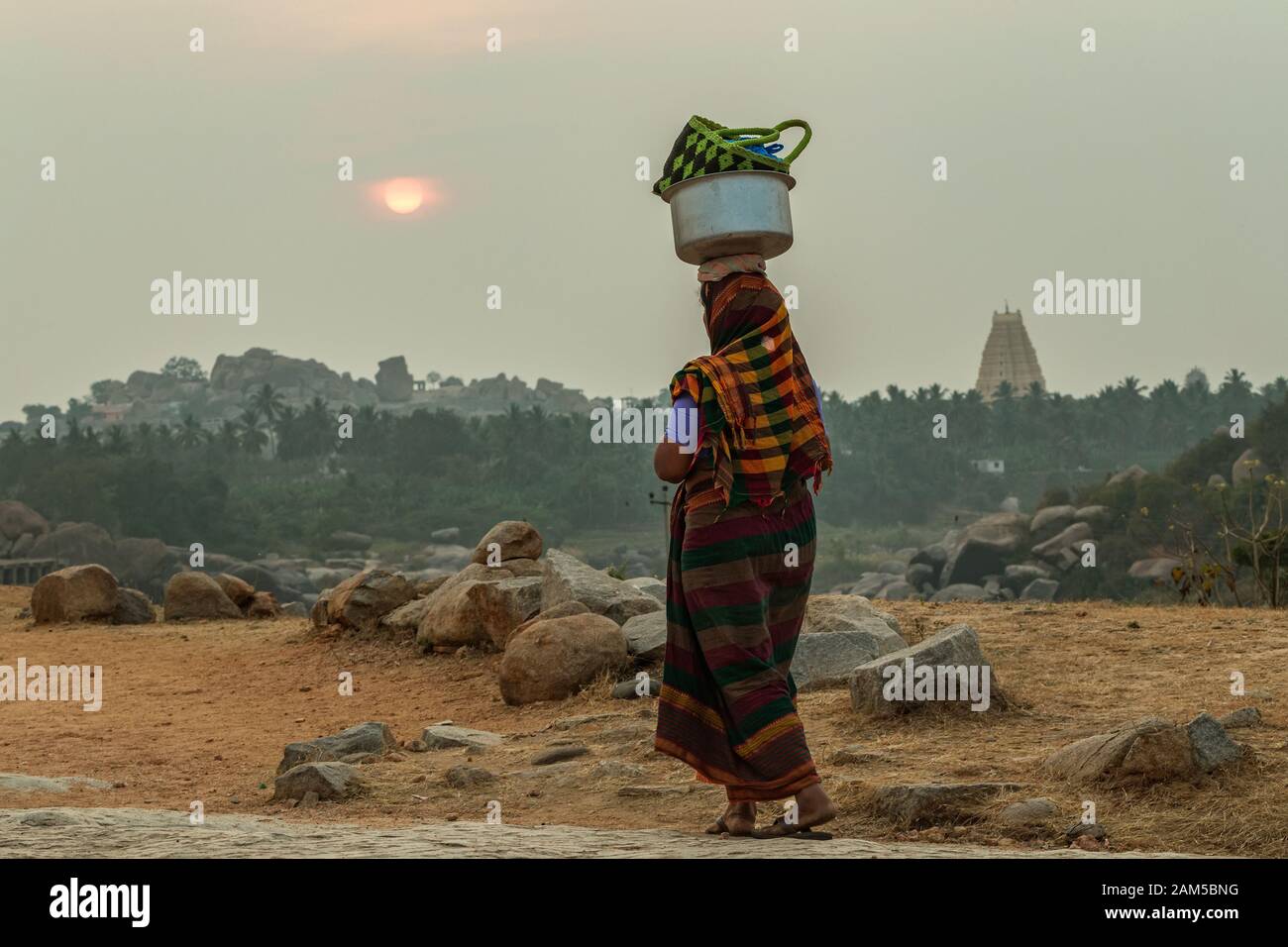 Una donna indiana trasporta un carico pesante sulla sua testa nella sera all'aperto. Il Gruppo dei Monumenti di Hampi. Karnataka Foto Stock