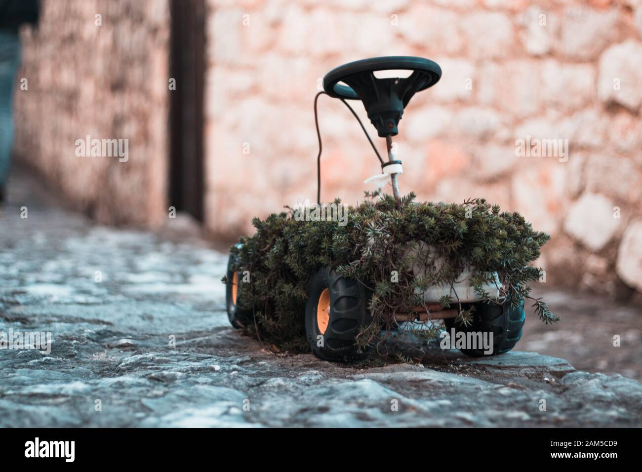 Strana piccola childrens vecchia auto giocattolo con pneumatici e di un volante di sterzo utilizzati come un vaso di fiori. Foto Stock