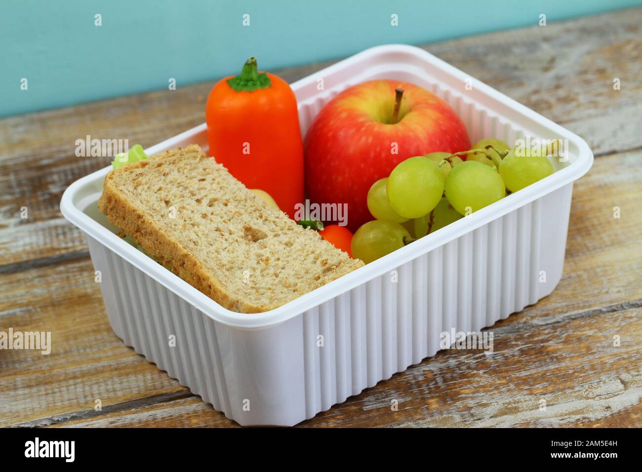 Portavivande sano e confezionato con sandwich di formaggio marrone, pepe giallo croccante e frutta fresca in scatola di plastica bianca Foto Stock