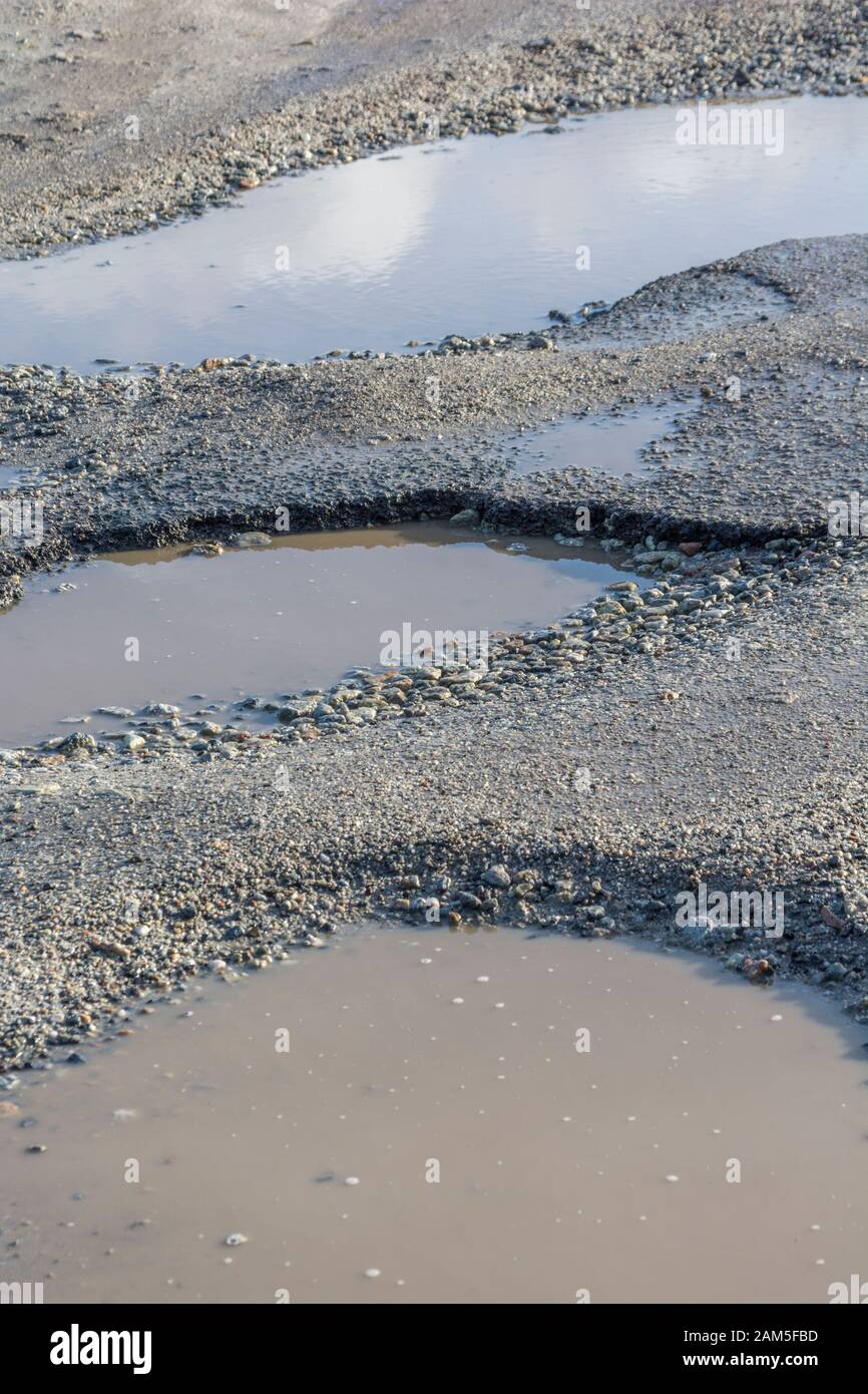 Grandi buche con pozze d'acqua in piedi in un parcheggio sul mare della Cornovaglia. Superficie irregolare metafora, superficie irregolare, in cattive condizioni, da riparare. Foto Stock