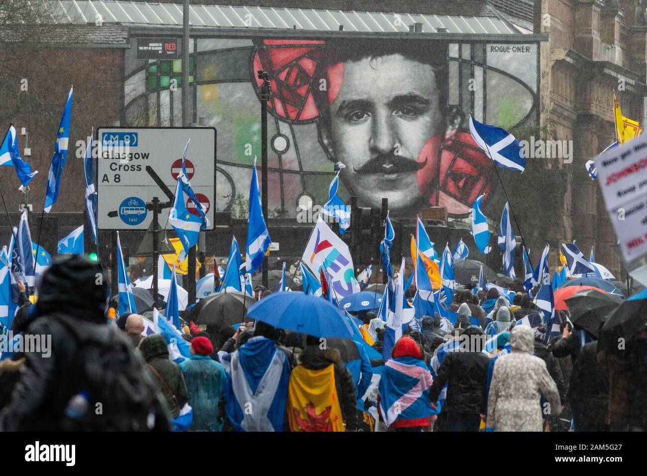 Glasgow, Scozia, Regno Unito - 11 gennaio 2020: Migliaia di sostenitori dell'indipendenza marciano per le strade di Glasgow nonostante la pioggia battente, qui passando davanti a un murale gigante di Charles Rennie Mackintosh Foto Stock