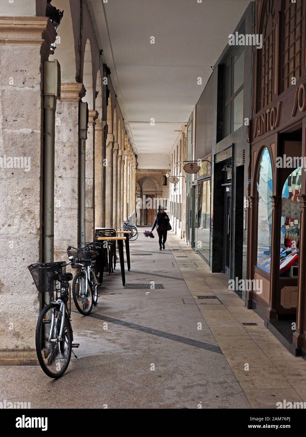 Femmina a piedi pedonale lungo coperto storica galleria shopping con le biciclette parcheggiate a fianco imponenti archi di pietra a Burgos, regione basca,Spagna Foto Stock
