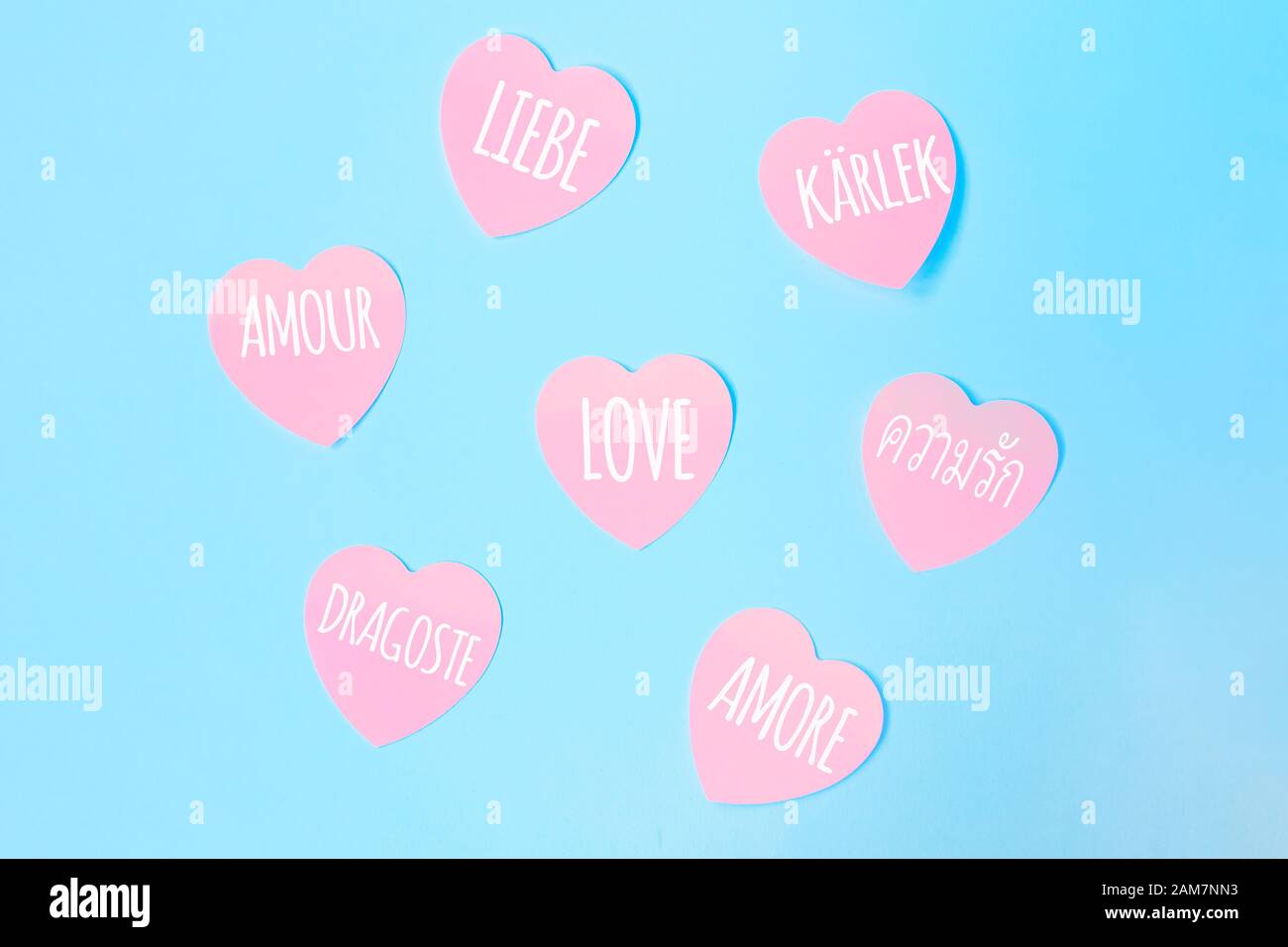 Alcune note adesive rosa a forma di cuore con la parola Love scritta in diverse lingue, come inglese, spagnolo, italiano, francese, olandese su sfondo blu. San Valentino, concetto di amore. Foto Stock