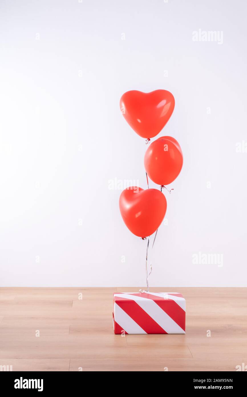 San Valentino, festa della mamma, concetto di design compleanno - Palloncino Cuore elio con scatola regalo su un pavimento in legno chiaro, sfondo bianco parete, primo piano. Foto Stock