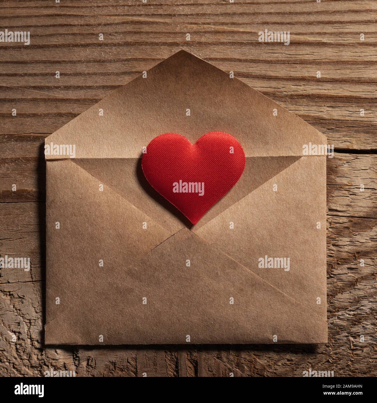 Il giorno di San Valentino lettera d'amore, busta di carta artigianale con cuore rosso su sfondo di legno Foto Stock