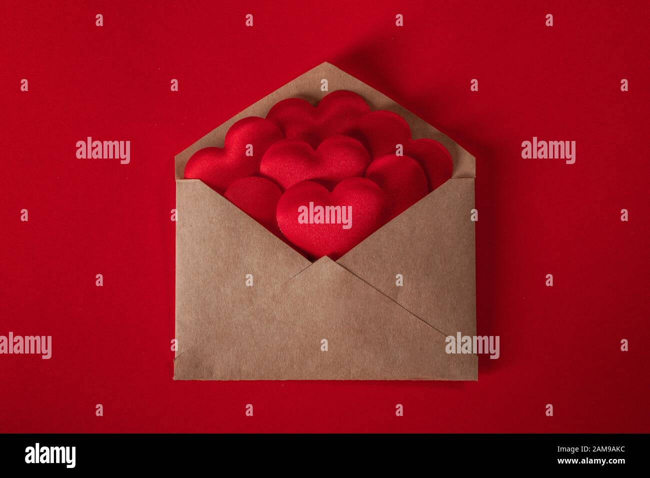 San Valentino lettera amore, busta di carta artigianale con cuore rosso mucchio diffuso su sfondo rosso. Foto Stock