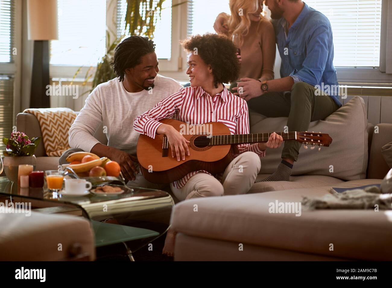 Coppia in amore divertirsi in camera con chitarra e amici Foto Stock