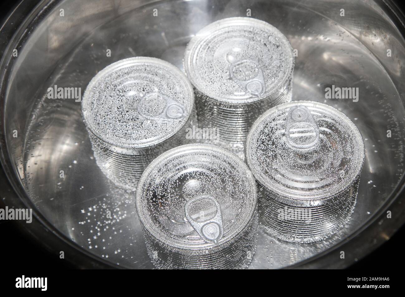 Quattro lattine chiuse sono bollenti all'interno della pentola grande. Simboleggia i processi di conservazione per ottenere una maggiore durata a magazzino. Foto Stock