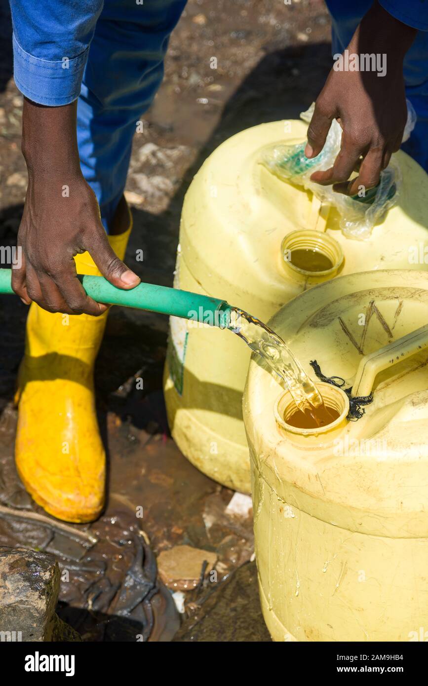 Un giovane uomo e alcuni ragazzi locali riempiono i contenitori d'acqua da un tubo d'acqua dolce, Korogocho slum, Nairobi, Kenya Foto Stock