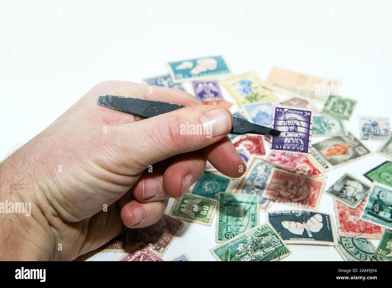Una mano tiene un timbro nella pinza. Diversi altri francobolli sono situati sotto. Philately è un hobby o anche un investimento. Foto Stock