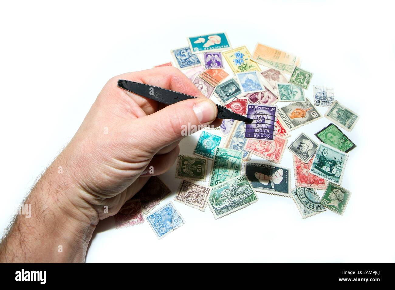 Una mano tiene un timbro nella pinza. Diversi altri francobolli sono situati sotto. Philately è un hobby o anche un investimento. Foto Stock