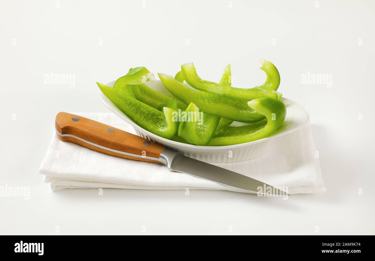 Affettare il peperone verde in una ciotola bianca e un coltello da cucina accanto Foto Stock