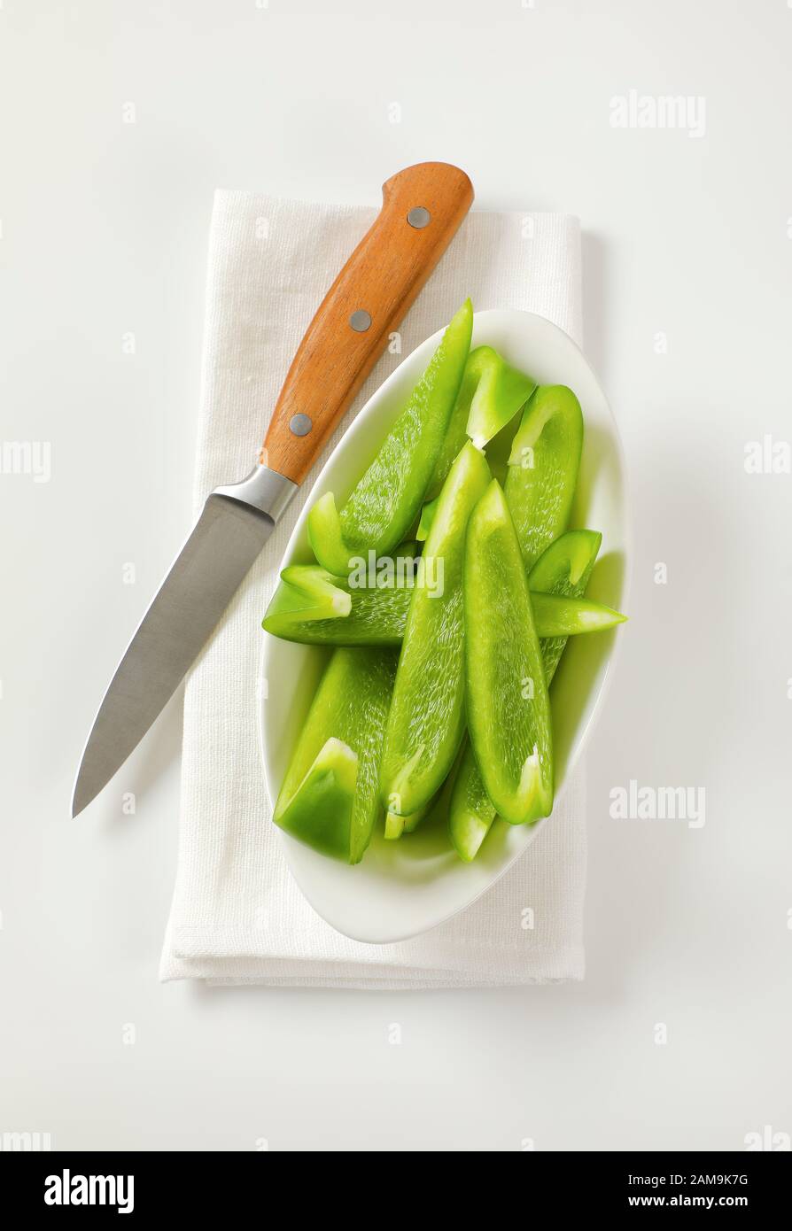 Affettare il peperone verde in una ciotola bianca e un coltello da cucina accanto Foto Stock