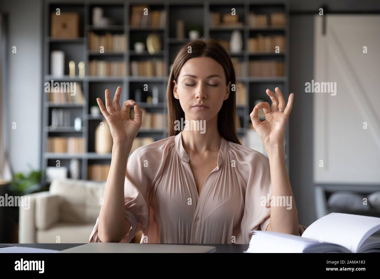 Calma giovane donna medita con gli occhi chiusi sul posto di lavoro Foto Stock