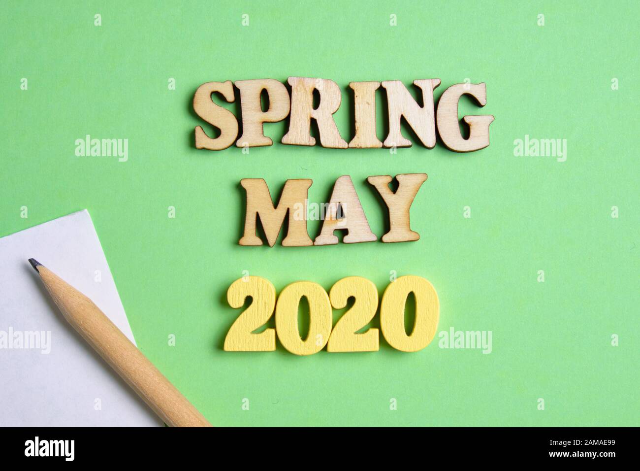Il concetto di primavera - maggio nel nuovo anno. Numeri di legno 2020 con lettere e foglio di carta con una matita su uno sfondo verde. Vista dall'alto. Chiudi Foto Stock