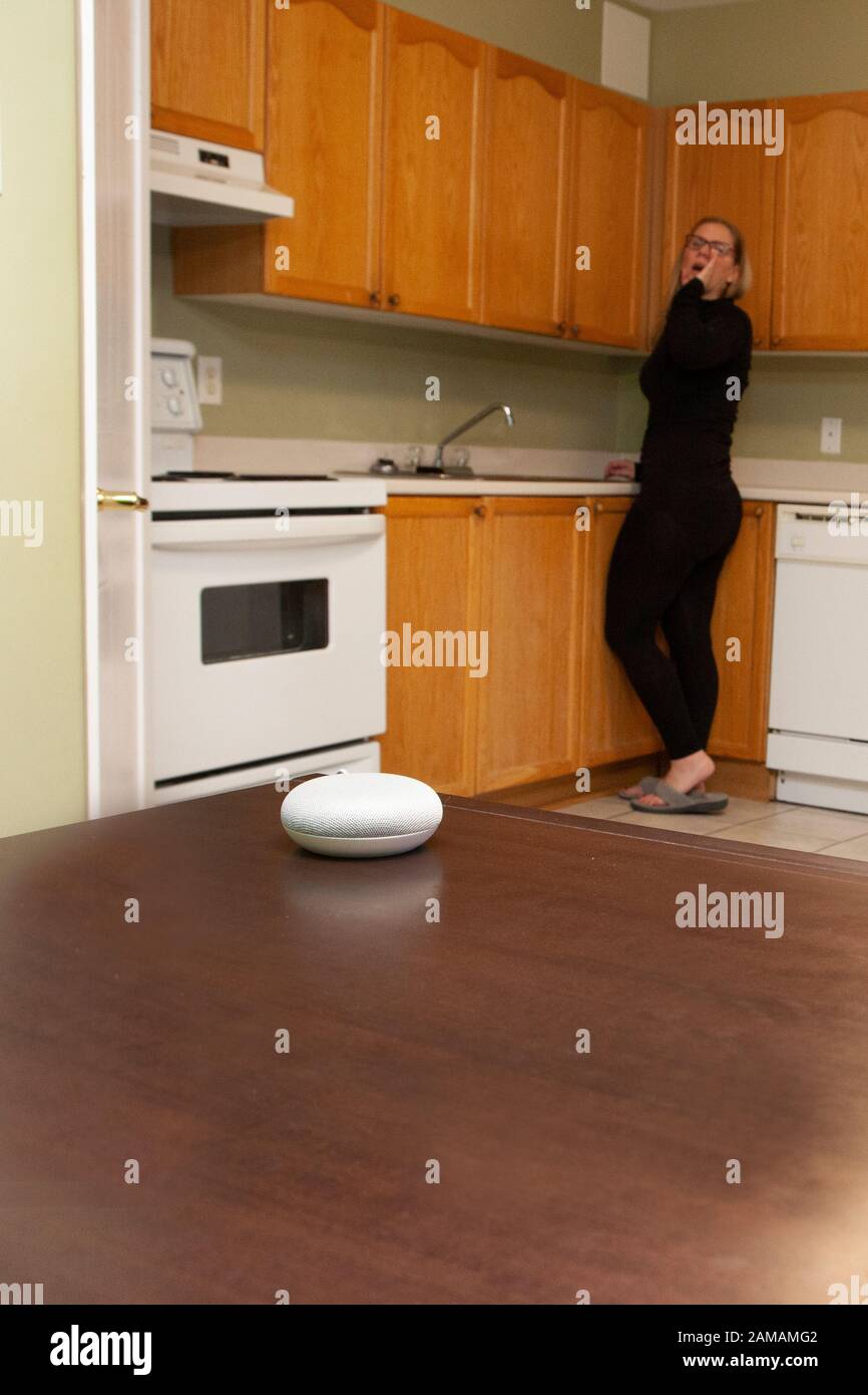 donna sullo sfondo della cucina che chiama il suo smart home mini altoparlante Foto Stock