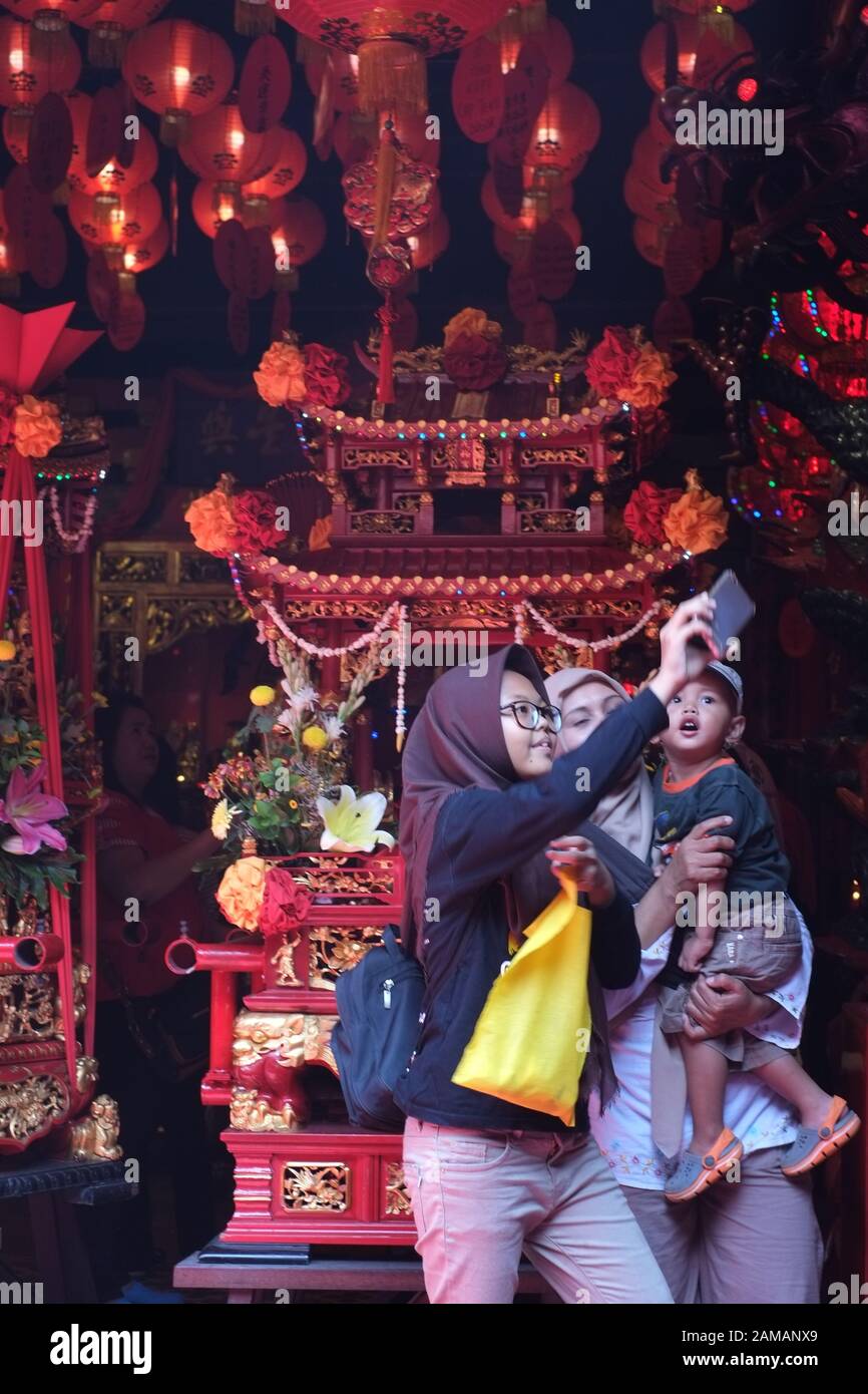 Due donne musulmane e un ragazzo di prendere un selfie foto utilizzando la fotocamera dello smartphone davanti di un buddista decorativo dio carrello nel nuovo anno cinese festival. Foto Stock