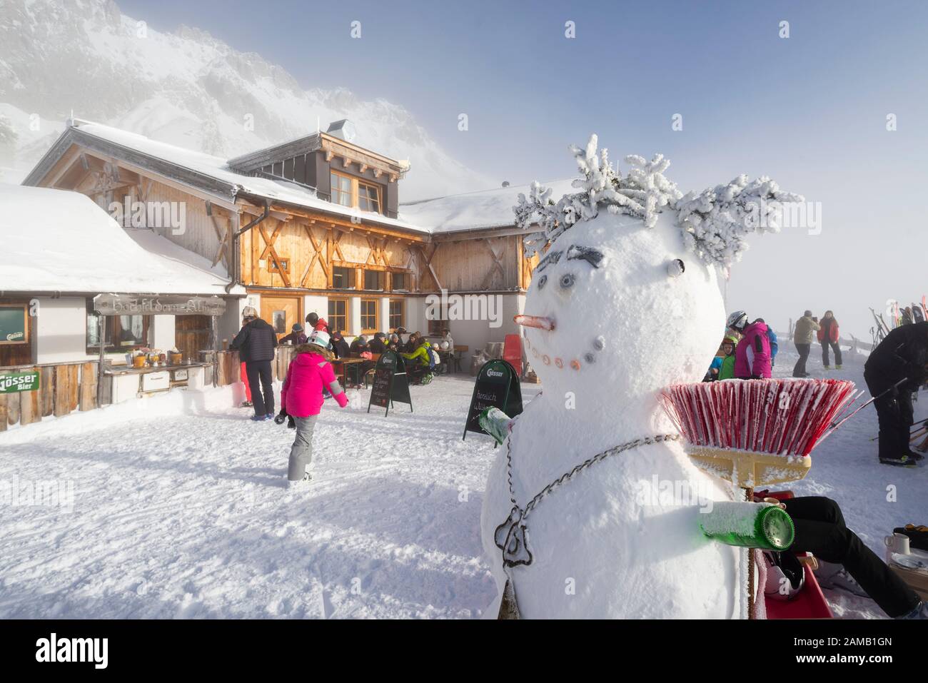 Snowman sulla terrazza soleggiata della baita innevata Hochfeldernalm, ristorante che accoglie gli sciatori nel comprensorio sciistico Ehrwalder Alm, Austria, Tirolo Foto Stock