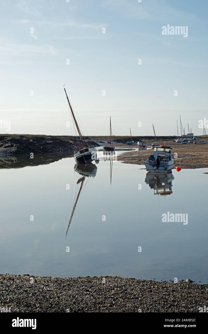 Tranquilla scena di yacht e barche a Brancaster Staithes a Norfolk in una giornata limpida e luminosa con riflessi catturati in acqua ferma Foto Stock