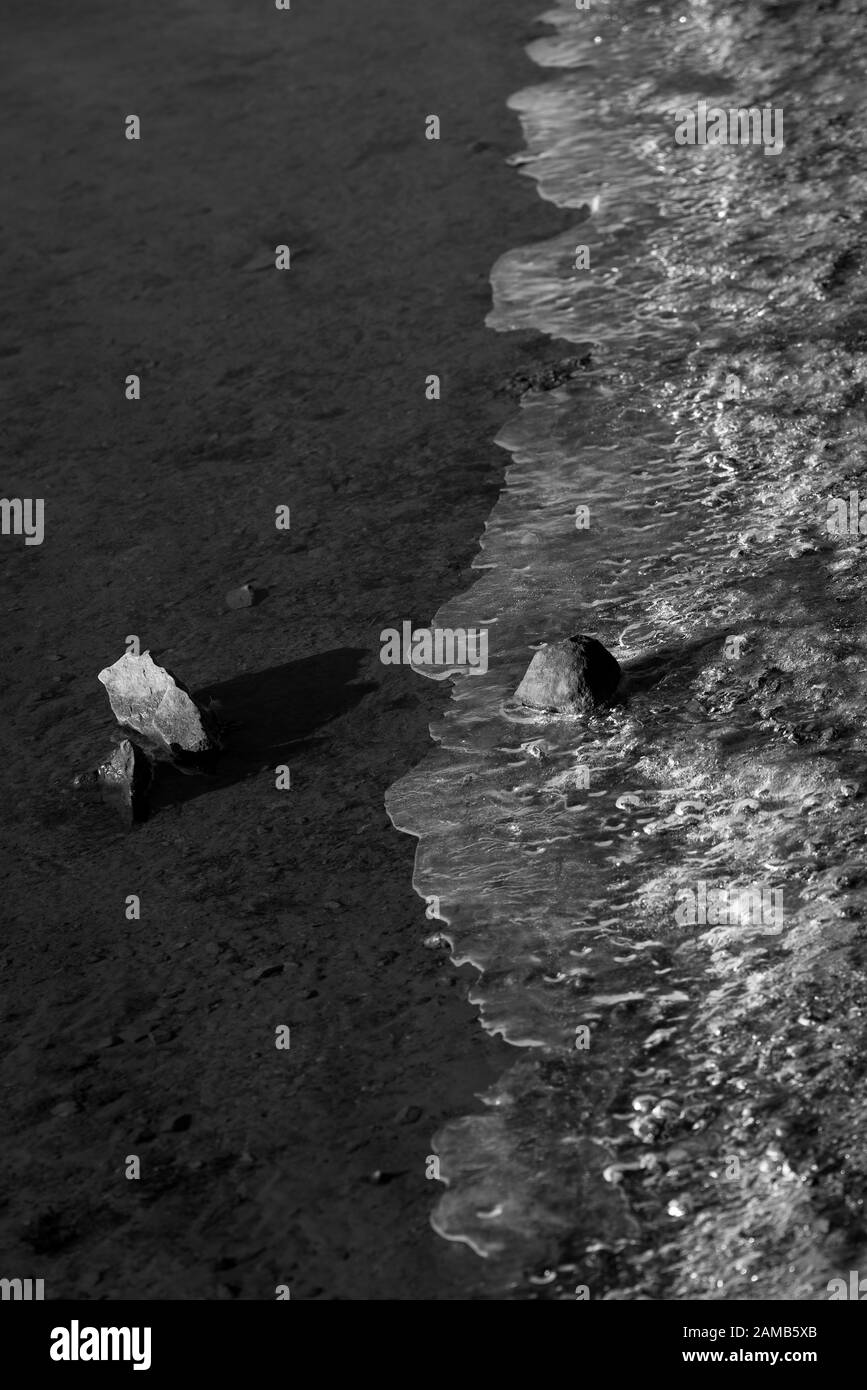 Un'immagine ravvicinata minimalista di pietre, acqua e ghiaccio catturati da un lago in un momento Foto Stock