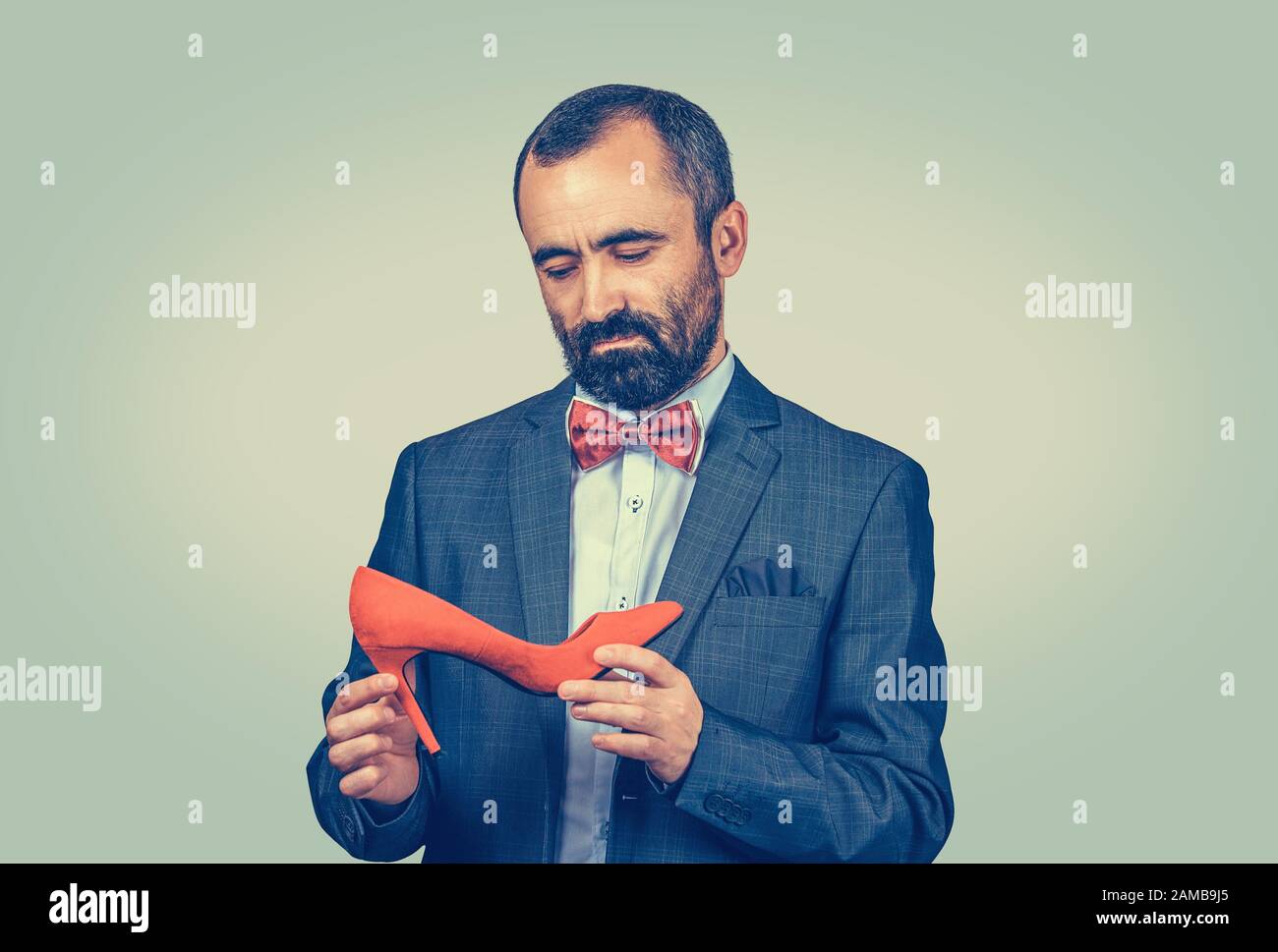 Uomo pensieroso che tiene e guarda alla scarpa rossa alta-heeled. Concetto di designer di scarpe. Corpo a mezza lunghezza. Una sola persona. Verde brillante giallo gr Foto Stock