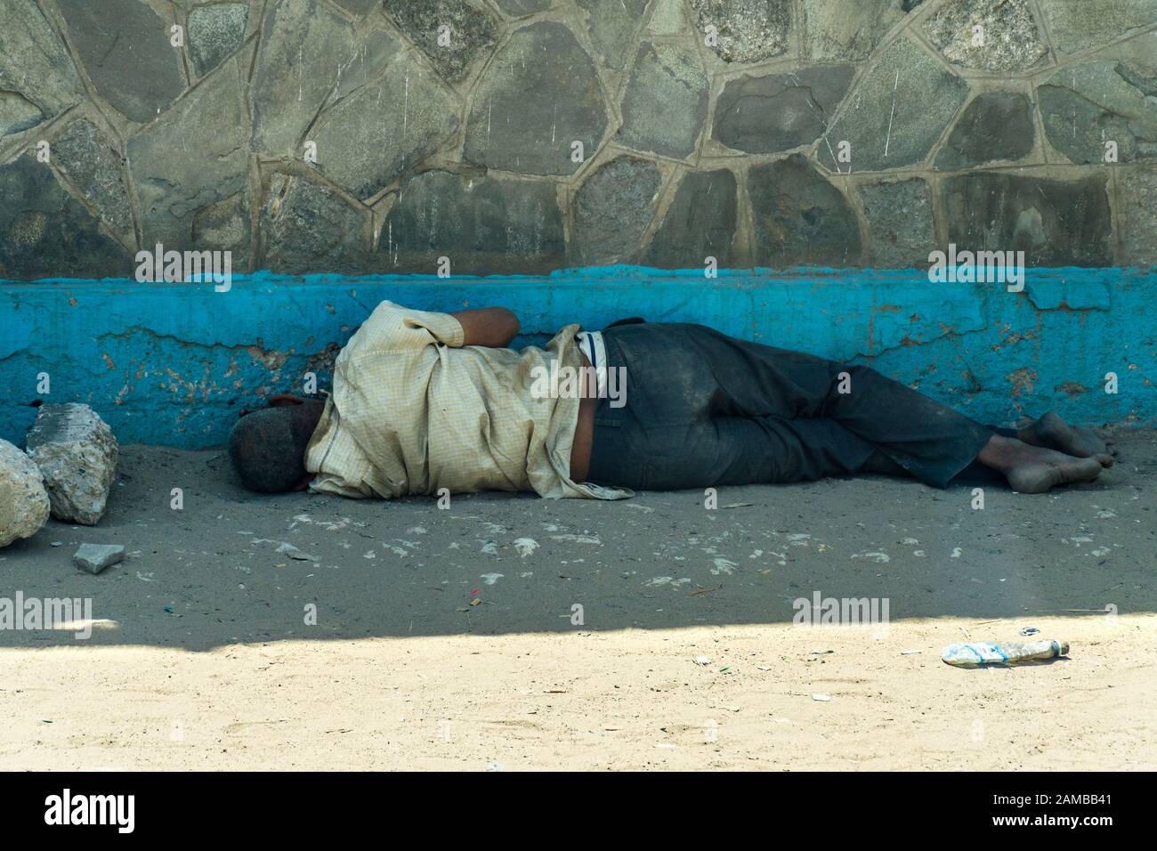 Un uomo keniota senza tetto dorme all'ombra di un edificio su un pavimento sabbioso e polveroso, Mombasa, Kenya Foto Stock