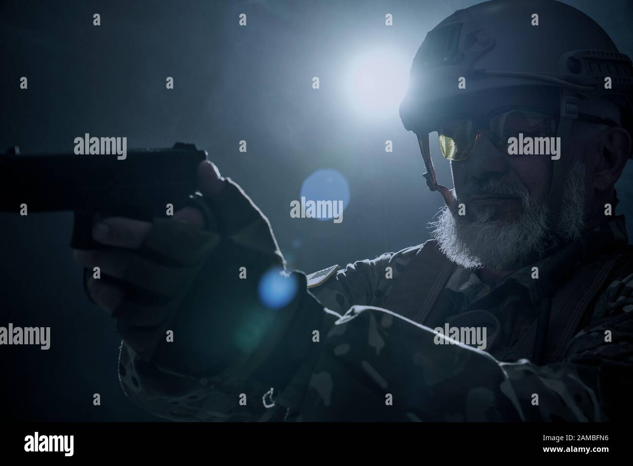 Primo piano di vecchio ufficiale militare che detiene una piccola pistola e mira. Ritratto di veterano bearded in uniforme camouflage e scatto del casco in atmosfera scura. Concetto di esercito, militare. Foto Stock