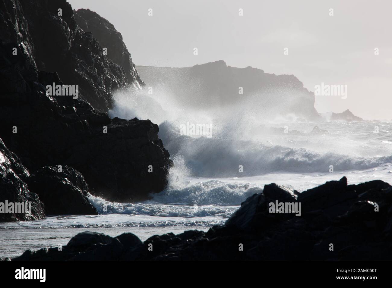 Le onde si infrangono contro le scogliere scure a Kynance Cove, in Cornovaglia Foto Stock